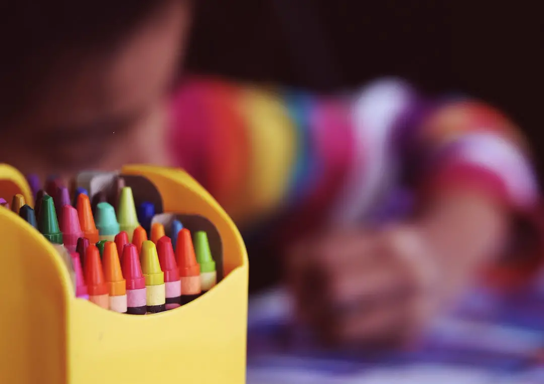 Crayons beside child coloring by Teacher Supply Store selective focal photo of crayons in yellow box